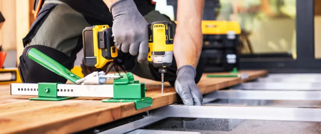 a deck builder using a yellow and black cordless drill_driver to fasten wooden planks onto a metal frame