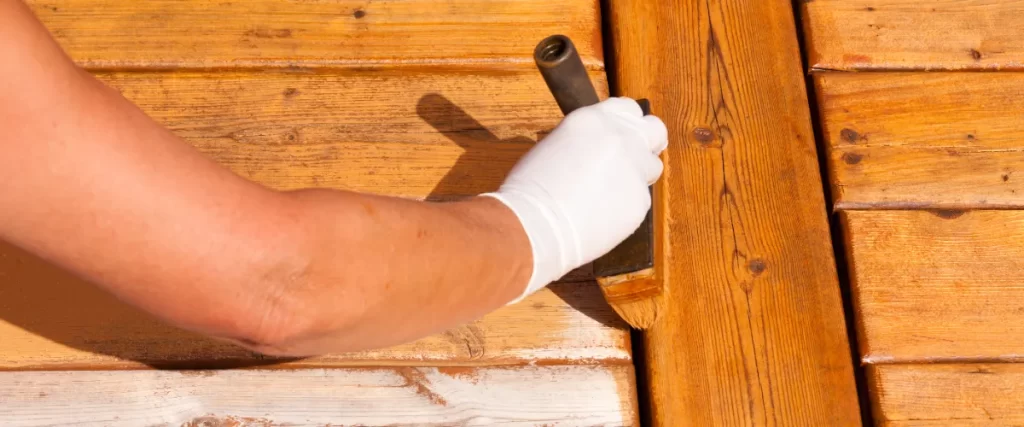 a person applying a protective finish, likely a wood stain or sealer, to a wooden deck