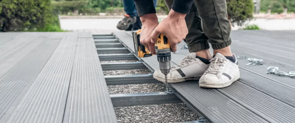 a worker using a cordless drill to install composite decking boards onto a metal subframe