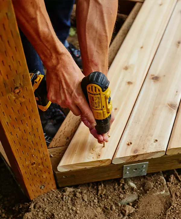 Close-up of a contractor's hands using a yellow power drill to install and secure new wooden boards during a deck repair in Nashville, TN.
