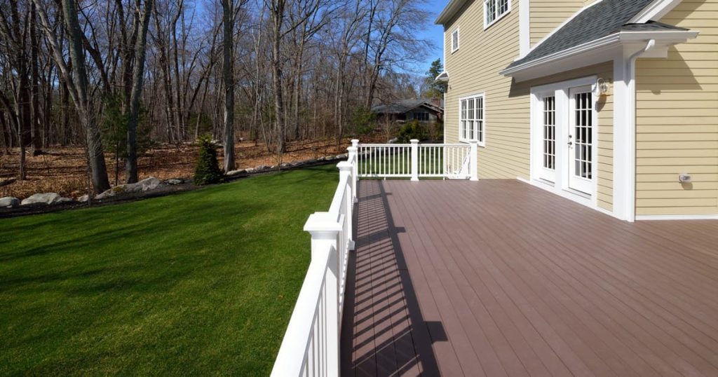 A clean, empty composite deck attached to a house with yellow siding and white railings, illustrating factors that impact deck cost Nashville TN.