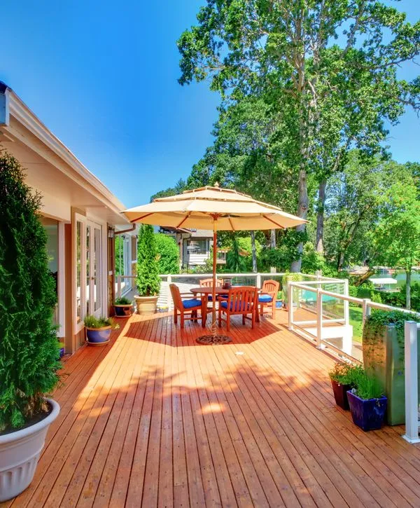 A spacious outdoor wooden deck built by a deck builder in Nashville, TN, featuring a dining table with a large umbrella, modern glass railings, and a scenic lake view.