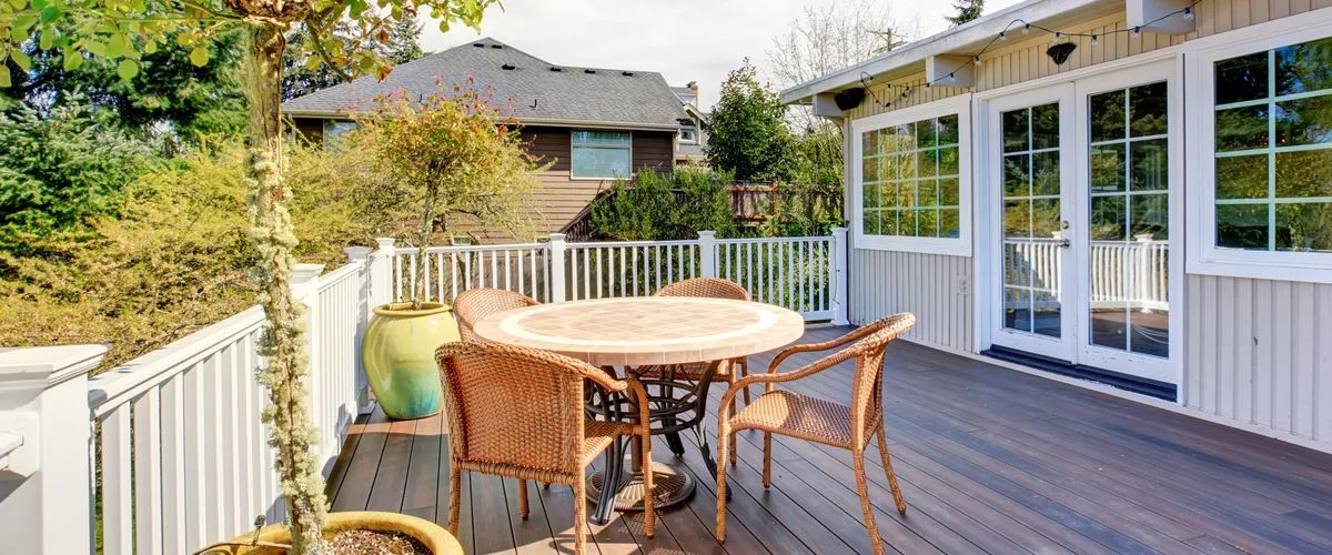 Elevated backyard deck featuring white perimeter railings, dark wood-grain planks, and a wicker dining set.