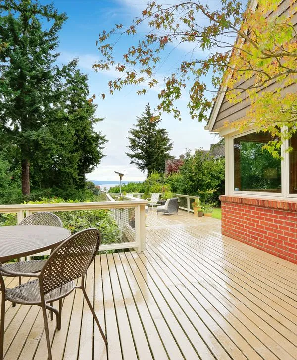 A beautiful completed deck replacement in Nashville featuring light decking, metal patio furniture, a red brick half-wall, and a scenic water view surrounded by tall trees.