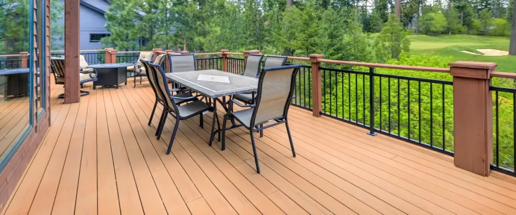 A wooden deck featuring black metal railings, an outdoor dining table with chairs, and a fire pit area overlooking a lush green golf course landscape.
