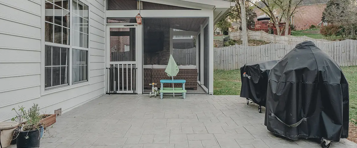 Stamped concrete patio with screened porch addition and outdoor grilling area in residential backyard